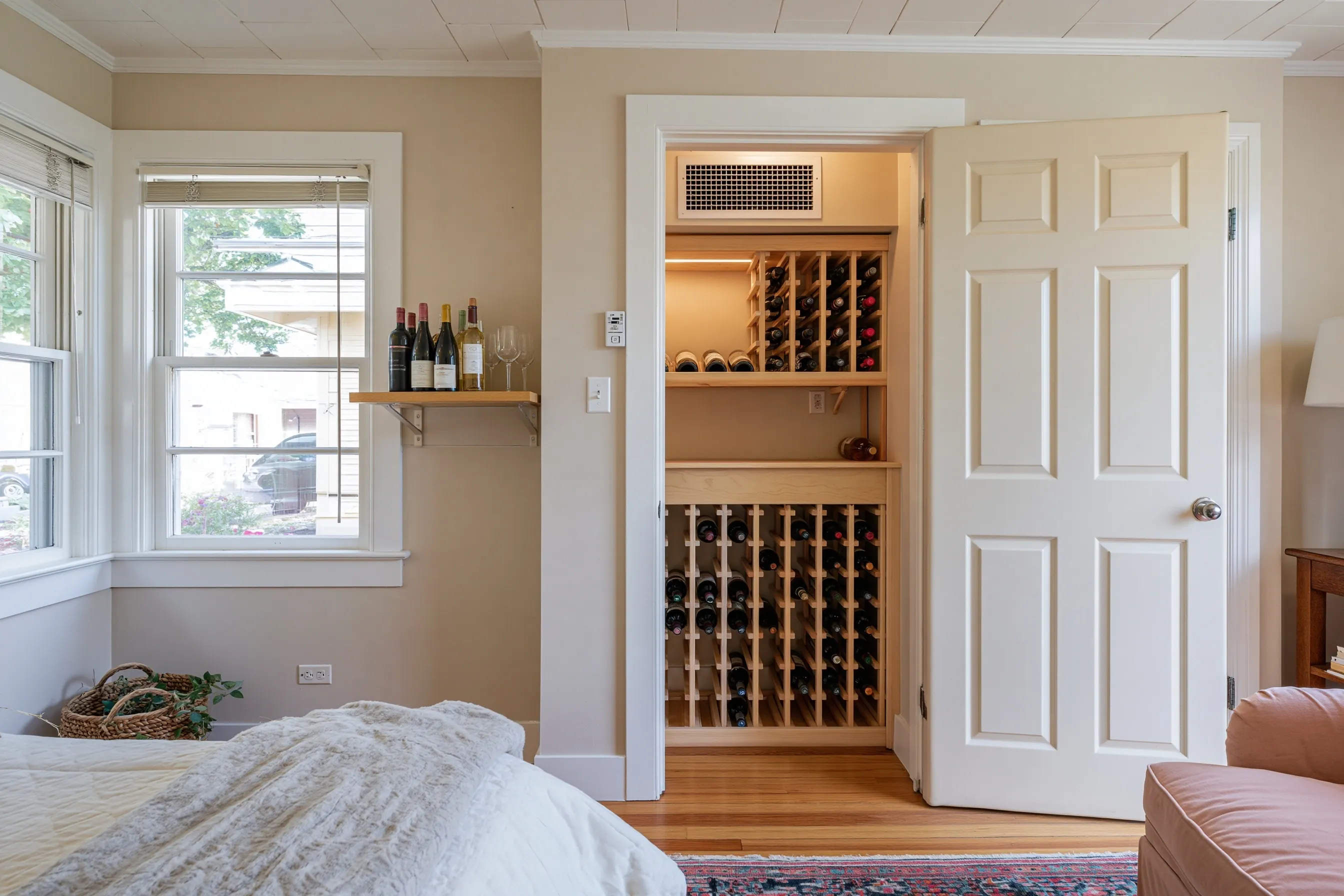 Reach-in closet in a guest bedroom, its panel door open on single-slot wood racks, a waist-high shelf and a cooling grille near the ceiling